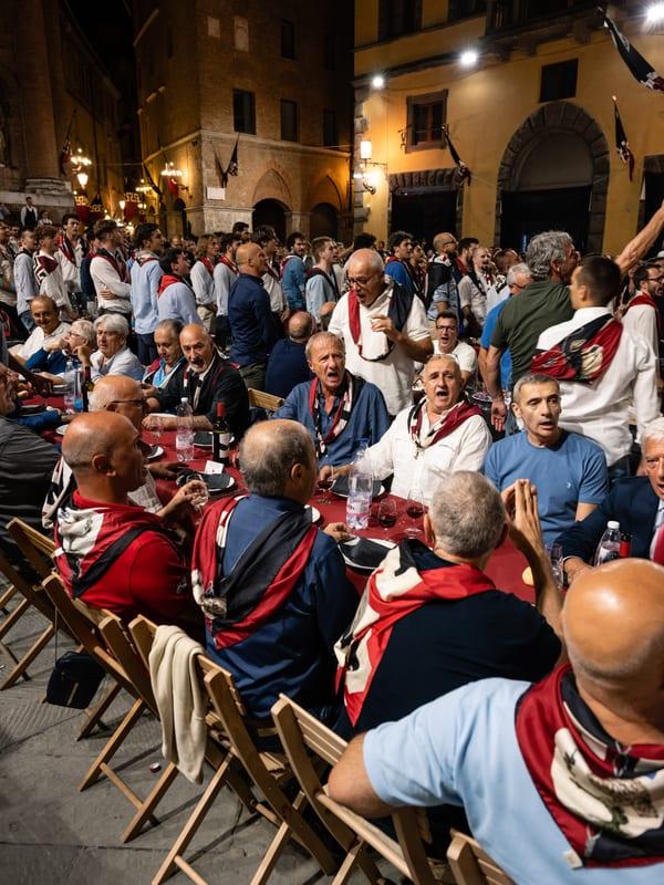 Members of a Siena contrada gathered at a long communal table, singing together the night before the Palio
